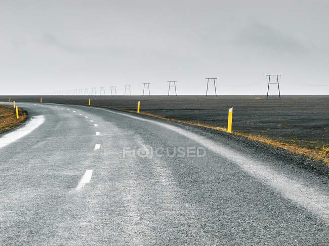 Paisaje plano con pilones y carretera rural, Dyrholaey, Islandia - foto de stock