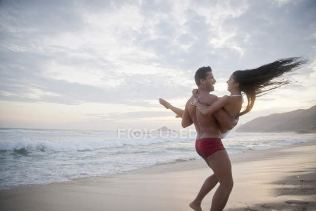 Coppia adulta sulla spiaggia, uomo con donna in braccio, vista posteriore — Foto stock