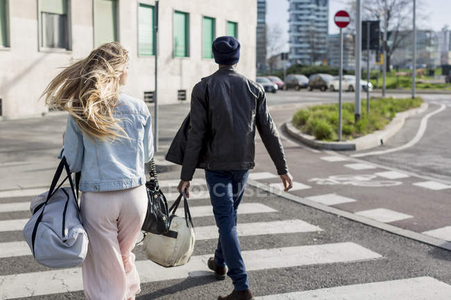 Rückansicht von Mann und Frau, die Straße überqueren und Taschen tragen — Stockfoto