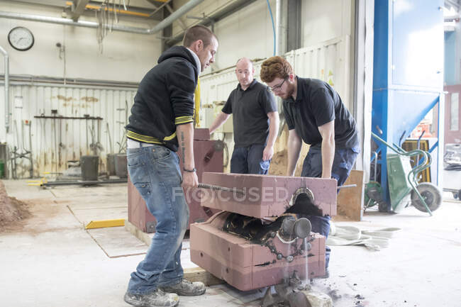 Male foundry workers lifting mould from bronze sculpture in bronze foundry — Stock Photo