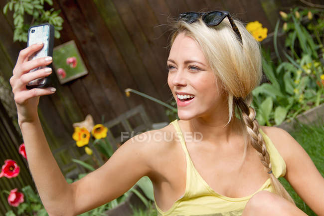 Young woman in garden taking selfie on smartphone — Stock Photo