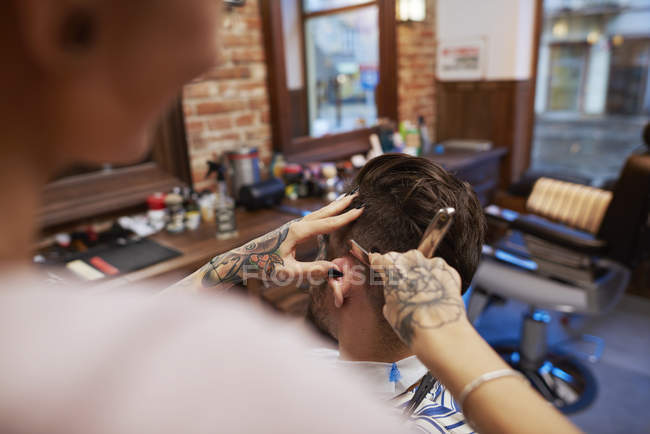 Hairdresser shaving customer's hair with straight razor — Stock Photo