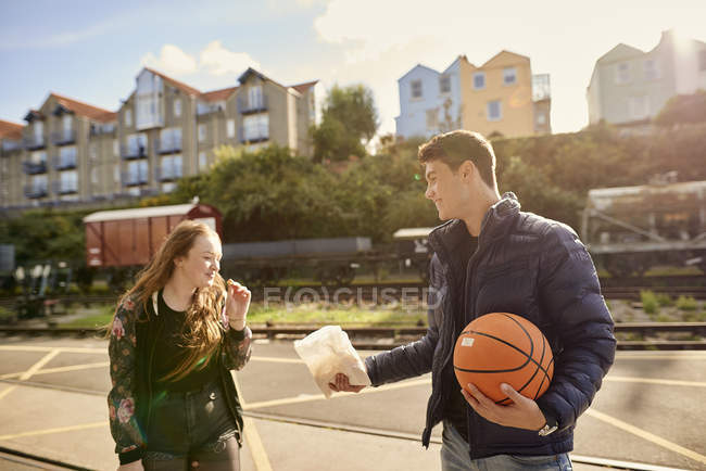 Юнак обміну пакетик чіпсів з другом, молодий чоловік тримає баскетбол, Брістоль, Великобританія — стокове фото