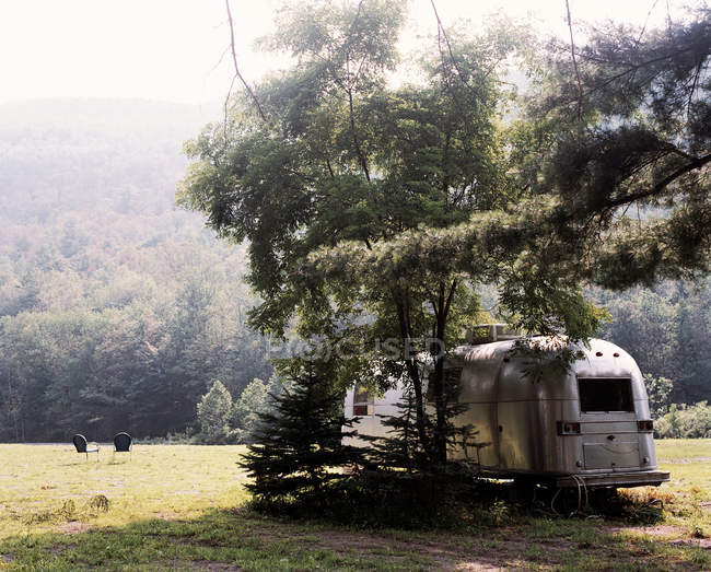 Трейлер, припаркований під деревом у полі — стокове фото