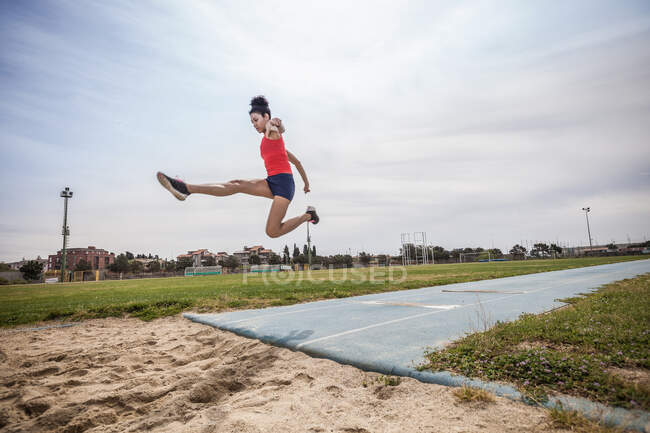 Jovem saltador longo feminino pulando no ar nas instalações esportivas — Fotografia de Stock