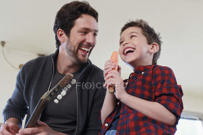 Padre e hijo con micrófono de guitarra y zanahoria - foto de stock