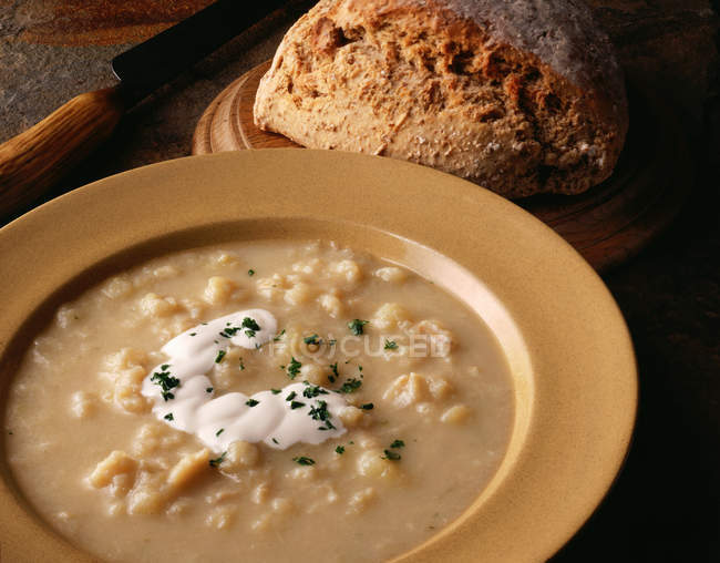 Sopa cullen skink con crema y hierbas picadas servido pan en la mesa - foto de stock