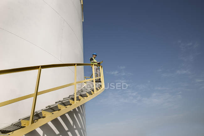 Maschio lavoratore in piedi su gradini del contenitore di stoccaggio presso il deposito di carburante, vista a basso angolo — Foto stock