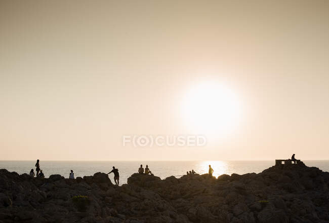 Silhouette de personnes sur des rochers au coucher du soleil, Ciutadella, Minorque, Espagne — Photo de stock