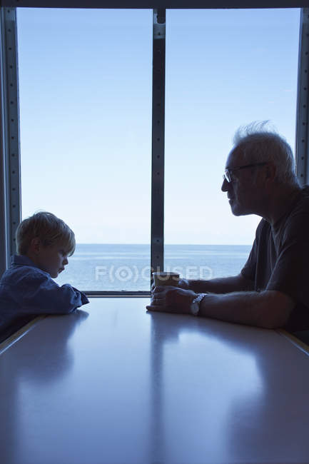 Мальчик и дедушка сидят за столом на пароме — стоковое фото