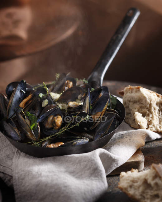 Mussels with herbs in frying pan and bread on table — Stock Photo