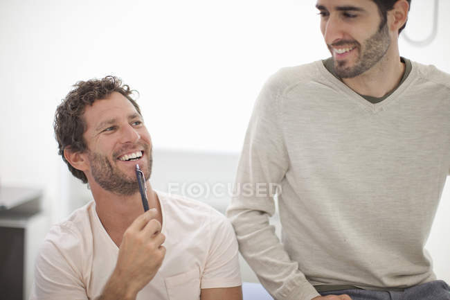 Dos colegas masculinos riendo en la oficina - foto de stock