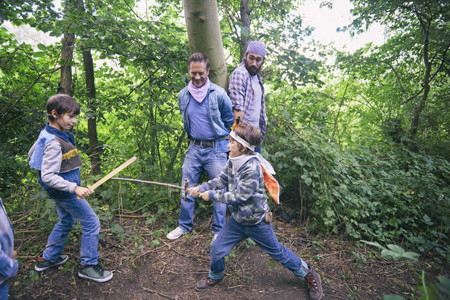 Two men captured whilst boys have sword fight in forest — Stock Photo