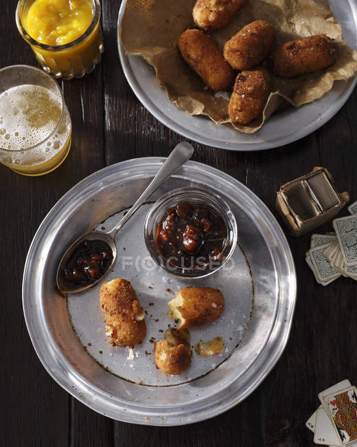 Vista dall'alto di piatti con crocchette, salse, bicchiere di birra e carte da gioco — Foto stock