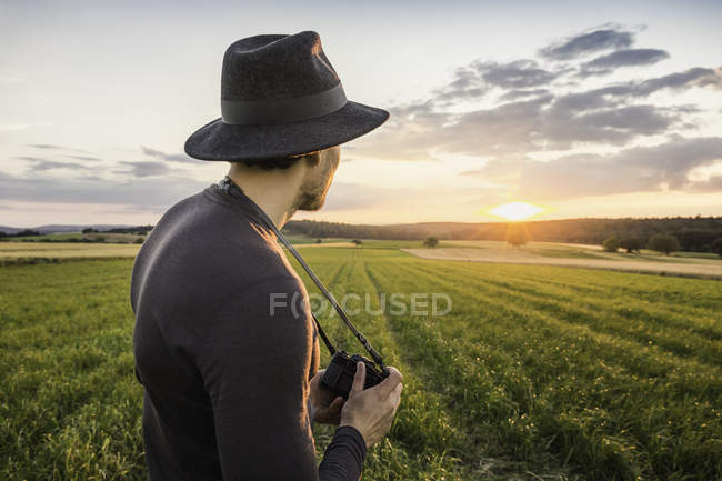 Portrait of mid adult man, standing in field, holding SLR camera, looking at view, Neulingen, Baden-Wurttemberg, Germany — Stock Photo