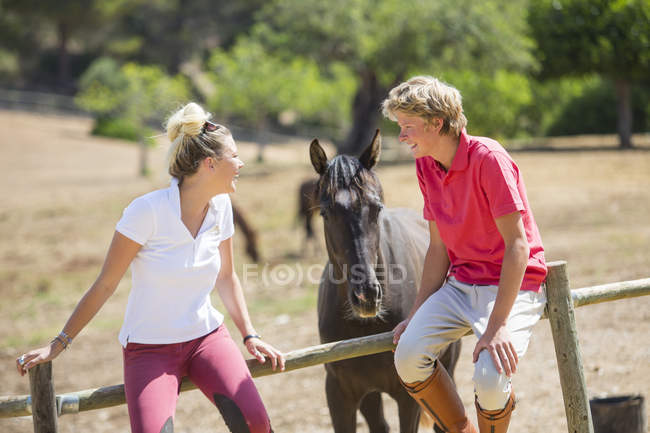 Young male and female grooms sitting on paddock fence at rural stables — Stock Photo