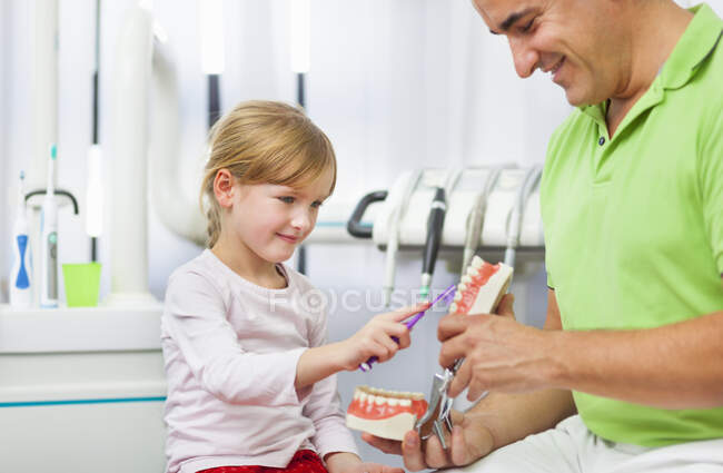 Дантист учит девушку чистить зубы — стоковое фото
