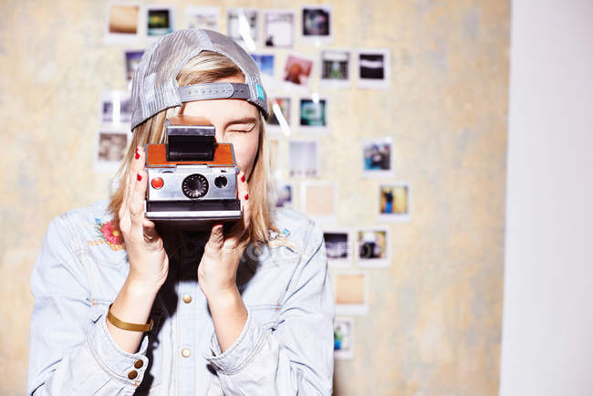 Jeune femme devant un mur photo prenant des photos sur un appareil photo rétro — Photo de stock