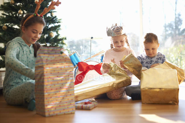 Хлопчик і сестри, сидячи на підлозі вітальні, відкривають різдвяні подарунки — стокове фото
