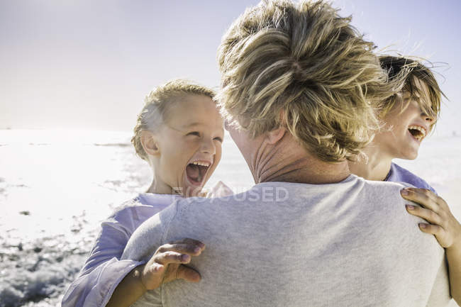 Pai carregando filhos em armas na praia — Fotografia de Stock