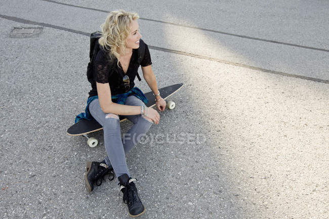 Жінка скейтбордистка сидить на скейтборді — стокове фото