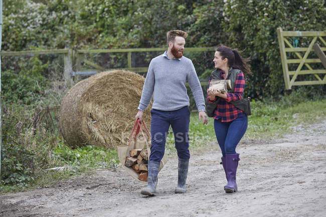 Couple on farmland carrying logs — Stock Photo