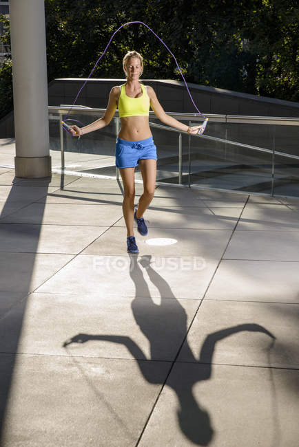 Jeune athlète féminine sautant en plein soleil urbain — Photo de stock