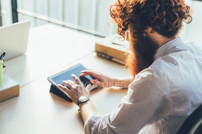 Junger männlicher Hipster mit roten Haaren und Bart am Schreibtisch mit digitalem Tablet-Touchscreen — Stockfoto