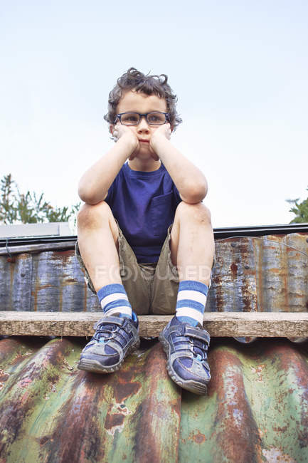 Glum little boy sitting on roof outdoors, head in hands — Stock Photo
