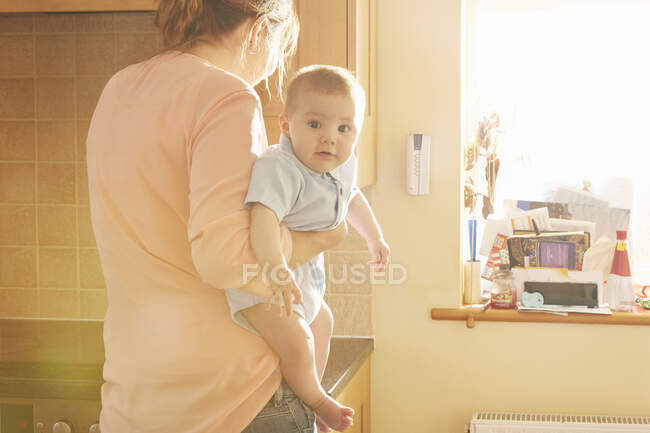 Mujer llevando a bebé hijo en brazos en la cocina - foto de stock