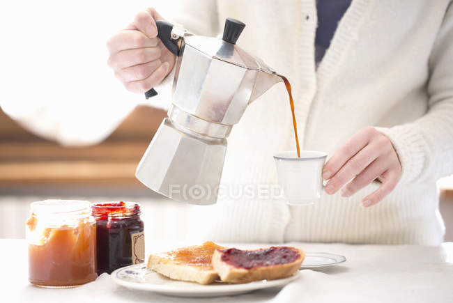 Cultivado disparo de mujer joven vertiendo café para el desayuno - foto de stock