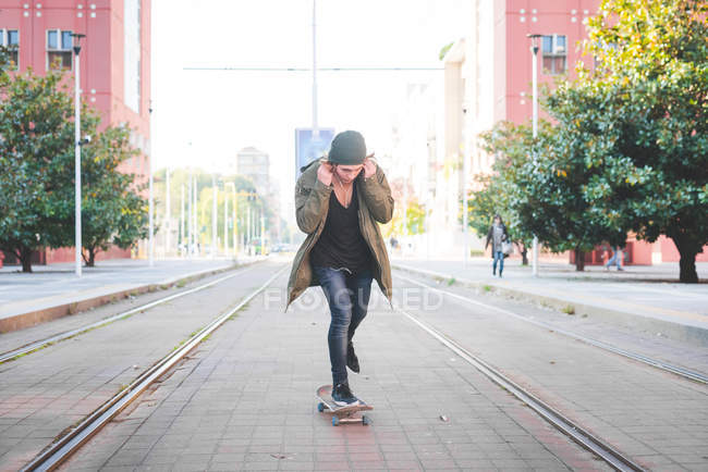 Junger männlicher Skateboarder justiert Kopfhörer beim Skateboarden in Straßenbahn — Stockfoto