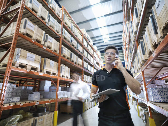 Worker using mobile phone and holding digital tablet in parts store in factory — Stock Photo