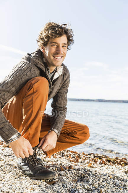 Hombre atando cordones en la orilla del lago - foto de stock