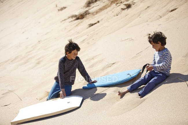Deux jeunes garçons assis sur une colline de sable avec des traîneaux à côté d'eux — Photo de stock