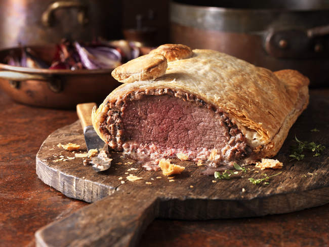 Rôti de bœuf wellington avec couteau sur planche de bois — Photo de stock