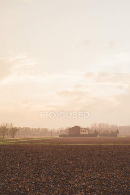 View of ploughed fields and distant farm buildings in mist — Stock Photo