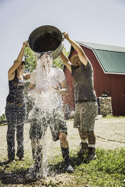 Farmworkers pouring water from metal bucket on friend — Stock Photo