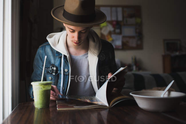 Young man sitting at table, having meal, reading magazine — Stock Photo