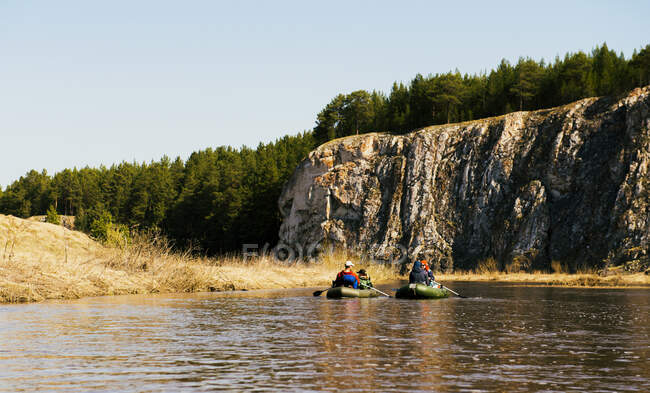 Group of friends on river in dinghies by rock face — Stock Photo