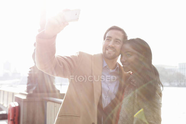 Пара стоїть біля річки, знімаючи власний портрет за допомогою смартфона — стокове фото