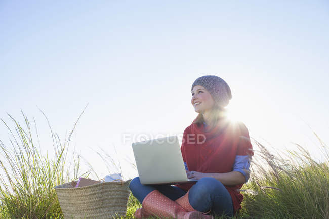 Молодая женщина сидит в длинной траве с ноутбуком — стоковое фото