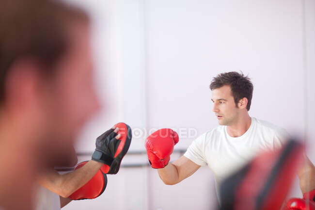 Young man and trainer boxing in sports hall — Stock Photo