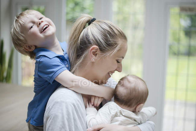 Joven, brazos alrededor del cuello de su madre, su madre abrazando al niño - foto de stock