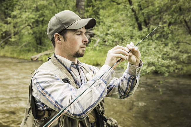 Homme par rivière préparant canne à pêche — Photo de stock