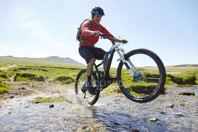 Cyclist doing wheelie through water — Stock Photo