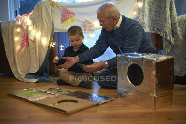 Boy and grandfather sitting on floor making robot costume — Stock Photo