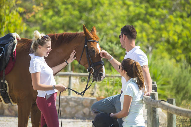 Female groom with horse and horse riders at rural stables — Stock Photo