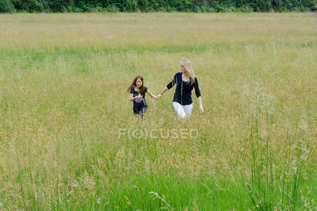 Madre e hija paseando por un largo campo de hierba - foto de stock