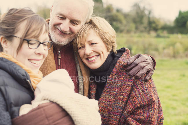 Madre sosteniendo hijo bebé, con abuelos en el prado - foto de stock